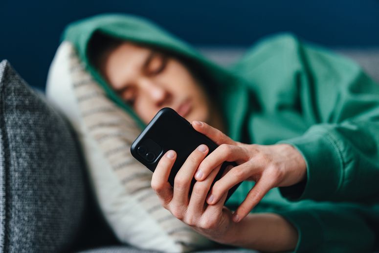 Un adolescente anónimo escribe mensajes de texto en su teléfono inteligente mientras está acostado en un sofá en su casa.
